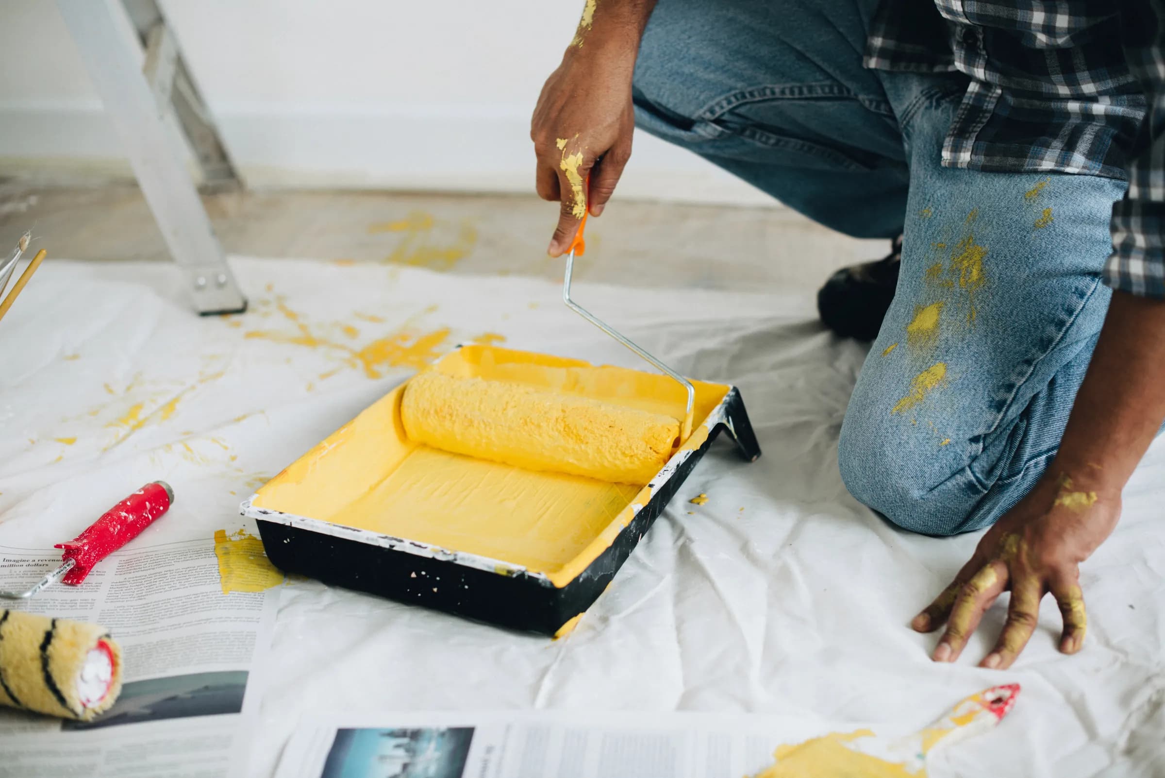 Painter loading a roller from a yellow paint tray on a protective drop cloth