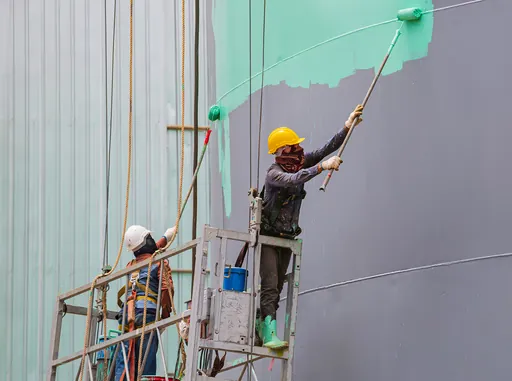 Two painters on a scaffold rolling mint paint onto a tall exterior wall